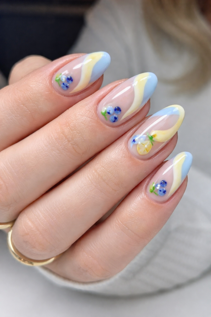 Soft butter yellow nails with cute cartoony lemon and blueberry nail art, playful spring nails palette with green leaf accents